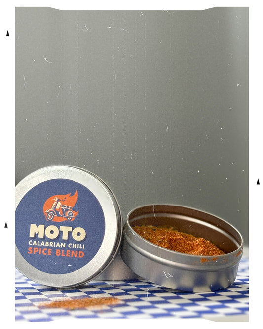 MOTO Calabrian Chili Spice Blend tin on a checkered surface with a gray background