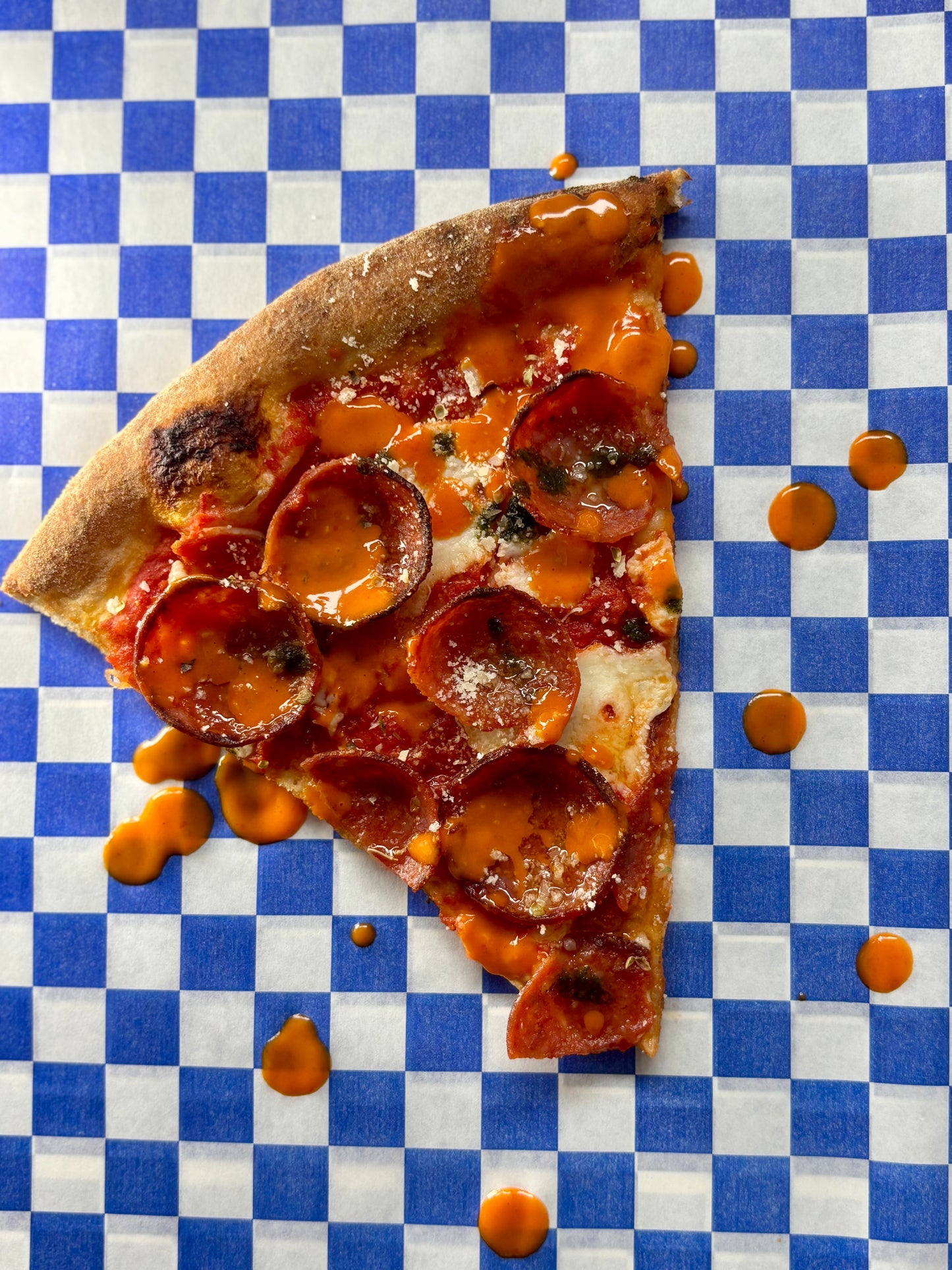 Slice of pepperoni and cheese pizza with MOTO Calabrian Chili Hot Sauce on a blue and white checkered background