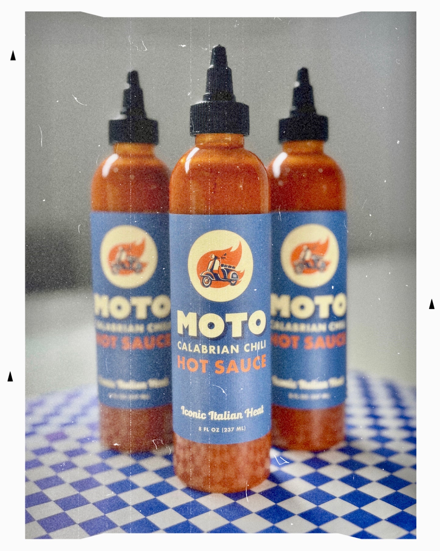 Three bottles of Moto Calabrian Chili Hot Sauce on a checkered surface