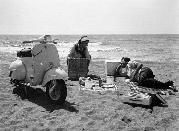 People with a Vespa scooter and picnic setup on a beach