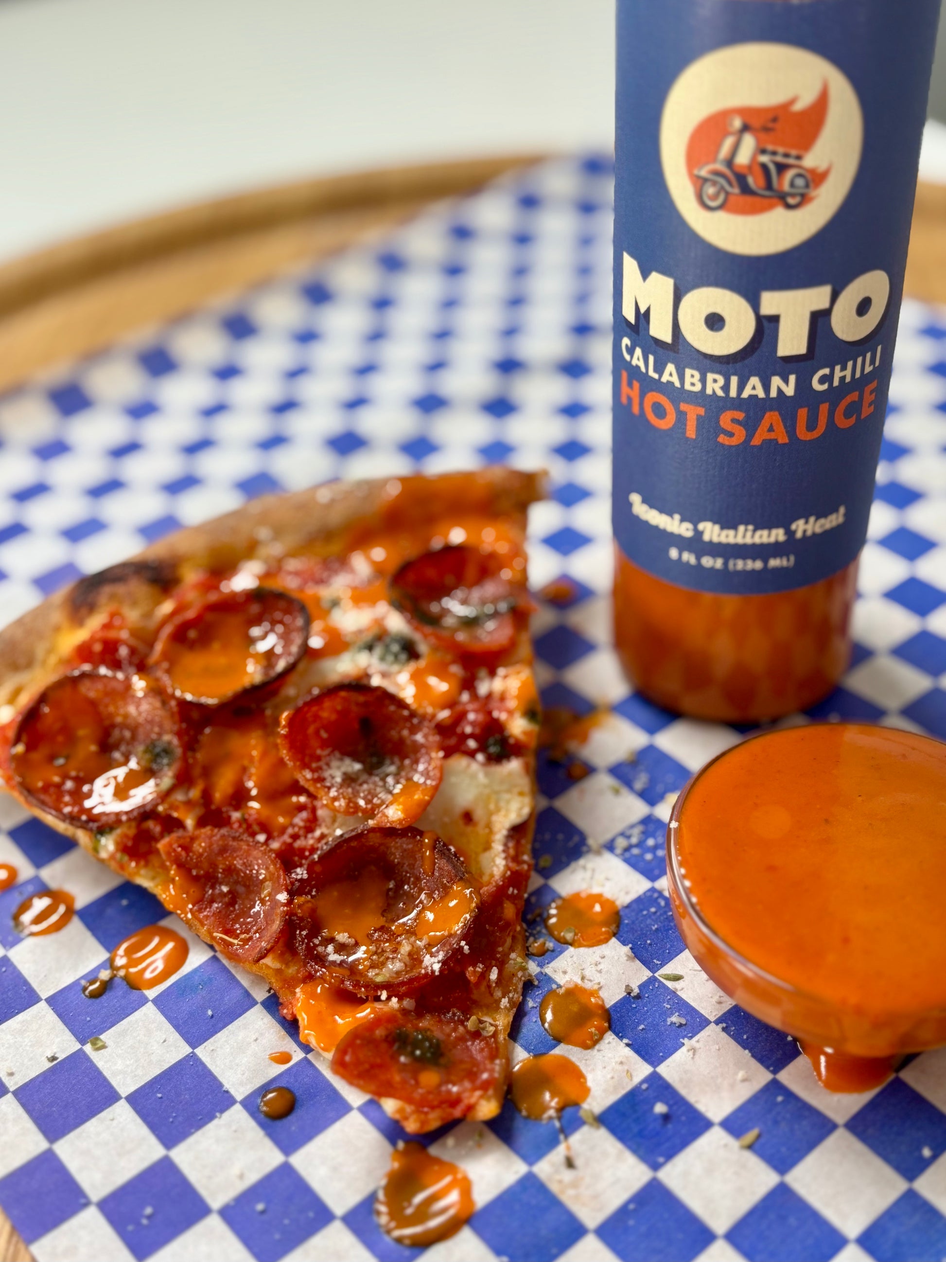 Slice of pizza with Moto Calabrian Chili Hot Sauce on a checkered tablecloth