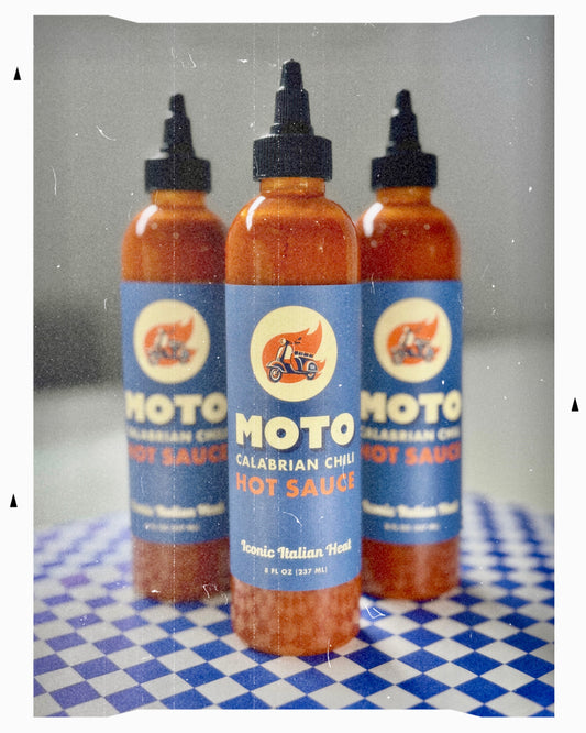 Three bottles of Moto Calabrian Chili Hot Sauce on a checkered surface