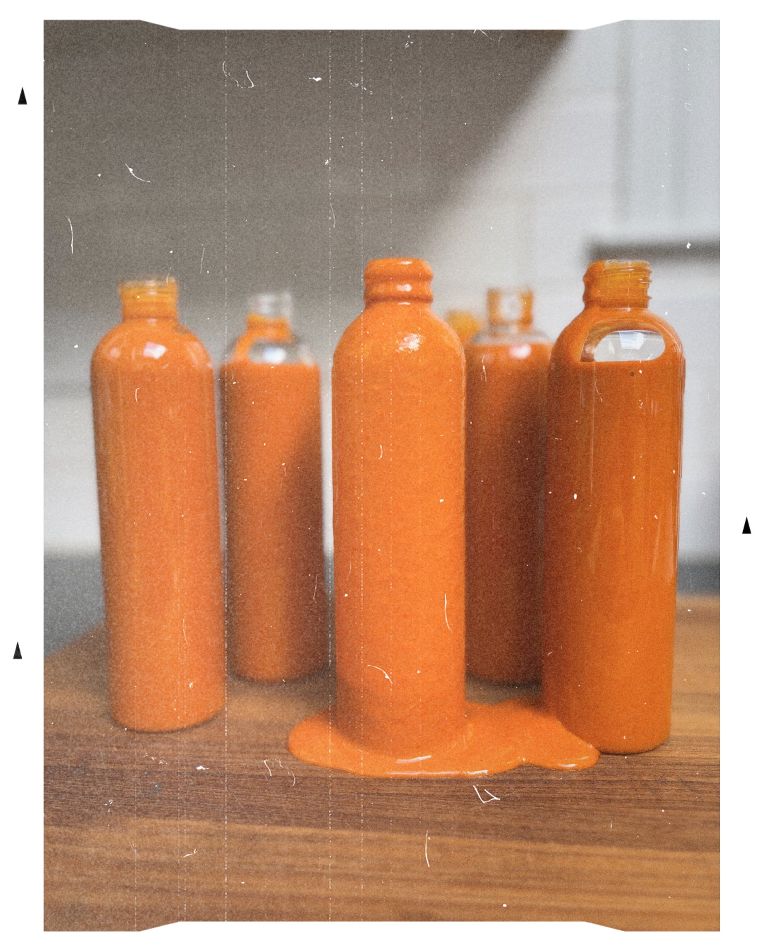 Set of orange bottles filled with MOTO Calabrian Chili Hot Sauce on a wooden surface with a gray background